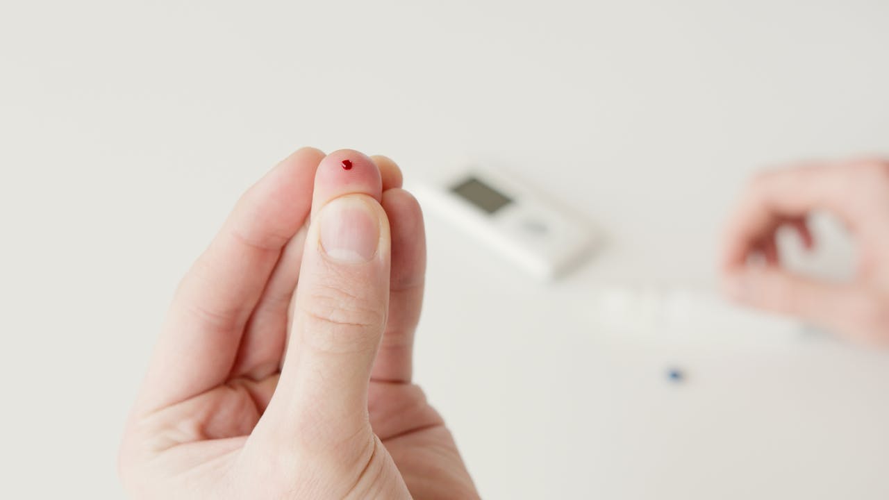 A close-up view of a hand with a blood drop, illustrating a diabetic blood sugar test.